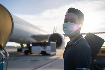 Asian man wearing face mask walks to stair entering airplane, parking at remote bay located outside...