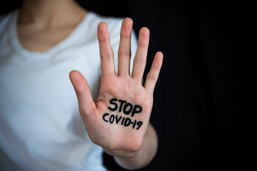 Woman holding out hand in stop gesture with Stop COVID-19 written on palm, with black background and copy space