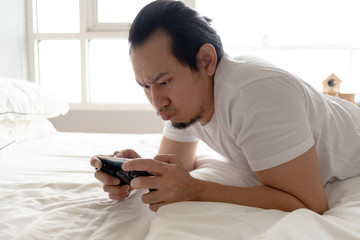 Sad and upset Asian man addicted to mobile game and losing it while stay at home.