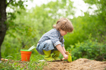 Boy on a farm with a garden tool digs the ground. Work