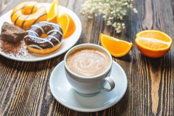 Bright appetizing Breakfast. A meal consisting of cup of natural black coffee with fresh orange, donuts with orange and chocolate. A beautiful summer Breakfast, a delicious start to the morning