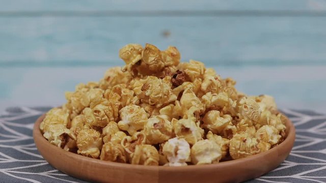 Caramel popcorn in a wooden plate  roating , Golden caramel popcorn closeup ,  Background of popcorn. Snacks and food for a movie 