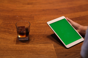 over shoulder of people using green screen tablet. a glass of iced drink on wooden table