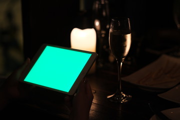 close up one hand showing green screen tablet in the bar at night. blurred glass of wine and candle light as background