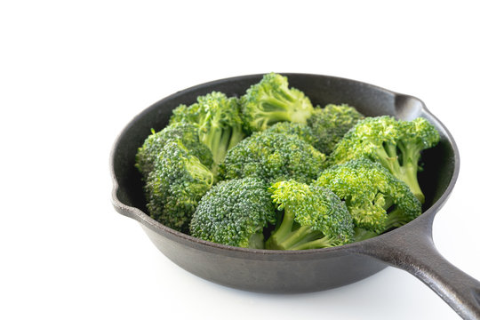 Broccoli florets in a frying pan close up isolated on white background.