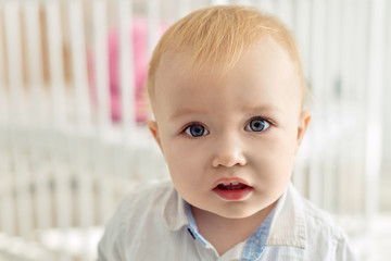 Boy and baby cot. Portrait of a beautiful fair-haired and light-eyed boy