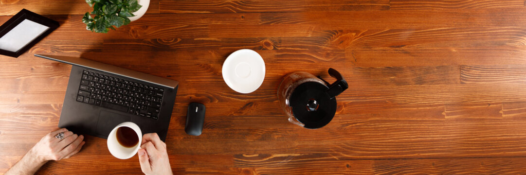 A Man Is Working By Using A Laptop Computer On Vintage Wooden Table. Hands On A Keyboard. Top View. Weekday Work Concept. Office Stuff And Gadgets Nearby.