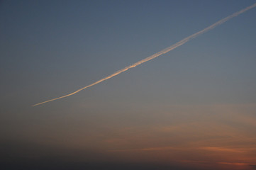 Fototapeta na wymiar 地平線に沈むきれいな夕日と飛行機雲
