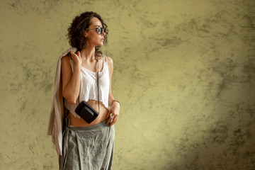 Obraz premium A girl with sunglasses and a camera against the wall. The concept of travel. Copy space