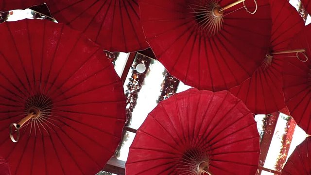 Traditional decorative umbrellas hanging under the roof of the building. A many red parasol is moving in wind under ceiling, Thailand.