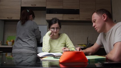 Family together in the kitchen, the father helps his daughter to perform lessons, mom to cook dinner. Helping parents