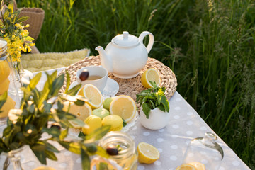 Tea concept, light cup with tea and white teapot decorated with lemons and oliva blooming yellow spring in the garden, top view. Teatime - Relax With Hot Tea In Zen Garden
