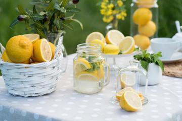 Lemonade with lemon, mint and ice on garden table. Preparation of the lemonade drink. Lemonade in the jug and lemons with mint on the table outdoor.