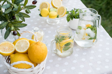 Lemonade with lemon, mint and ice on garden table. Preparation of the lemonade drink. Lemonade in the jug and lemons with mint on the table outdoor.