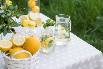 Lemonade with lemon, mint and ice on garden table. Preparation of the lemonade drink. Lemonade in the jug and lemons with mint on the table outdoor.