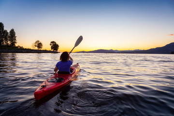 Girl Kayaking in Pacific Ocean during a vibrant golden sunny sunset. Taken in False Creek, Downtown Vancouver, British Columbia, Canada.