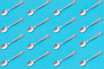 Metal dessert spoons with blue background. Repeat pattern.