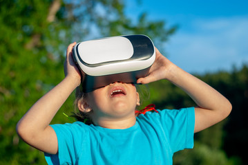 Little girl is looking into virtual reality glasses. The bright sun illuminates the girl. In the...