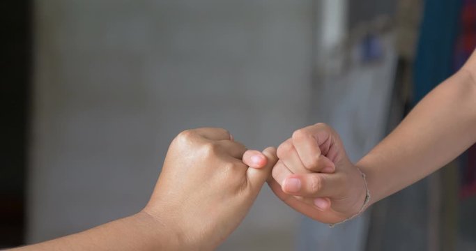 Close-up shot little finger hand of the girl and young woman be hand in hand, metaphor contract commitment, and promise, selective focus shallow depth of field