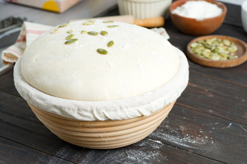 Homemade freshly prepared yeast dough in a basket for baking with pampkin seeds on a dark wooden background.