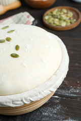 Homemade freshly prepared yeast dough in a basket for baking with pampkin seeds on a dark wooden background.
