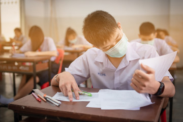 Obraz na płótnie Canvas An Asian high school students in a white school uniform wearing a mask to do final exams in the midst of Coronavirus disease 2019 (COVID-19) epidemic and PM 2.5.
