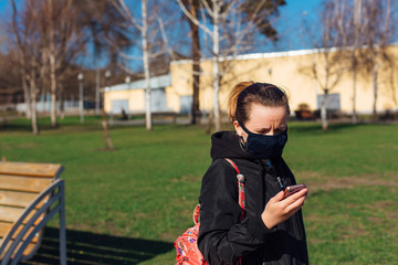 Woman wearing black fabric face mask holding mobile phone in hand. Concept of using medical mask to prevent the spread of germs, such as Coronavirus COVID-19.