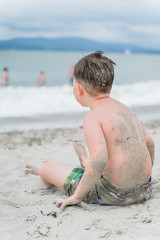in the foreground, a boy sits on the white sand and looks at the sea, in the background, the beach and the sea