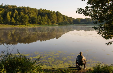 A man is fishing on a forest lake on a Sunny summer morning. Moscow region. Russia.
