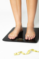 A girl is standing on the scales on a white background next to a centimeter. Close legs plan on the scales. Track changes in your weight. Losing weight.