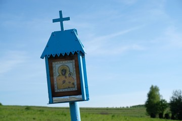 A small roadside blue chapel with the Mother of God among green fields. Polish countryside, Cracow-Czestochowa Upland, Poland.