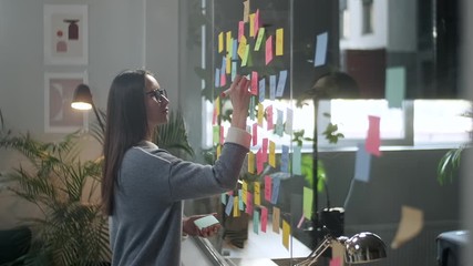 Young Business Woman Brainstorming. Asian Woman Writing Down Ideas On Sticky Notes Attached To Glass Wall. Business Success Concept - Powered by Adobe