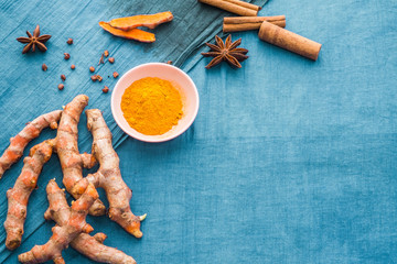 Top view ingredients dried spices with copy space on bright blue background. Organic turmeric curcumin fresh roots and powder, cinnamon and star anise to make natural herbal drink and healthy food