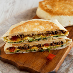 Tasty Homemade Beef Crunchwrap Quesadilla on a rustic wooden board, side view.