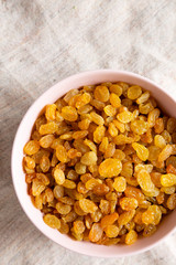 Golden Raisins in a Pink Bowl on cloth, top view. Flat lay, overhead, from above. Copy space.