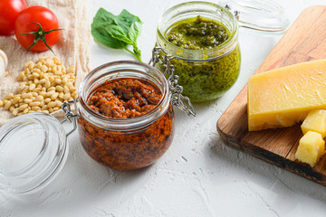Glass jars with red and green pesto and cooking ingredients Parmesan cheese, basil leaves, pine...