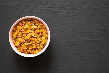 Golden Raisins in a Pink Bowl on a black background, top view. Flat lay, overhead, from above. Copy space.