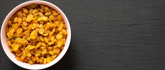 Golden Raisins in a Pink Bowl on a black background, top view. Flat lay, overhead, from above. Space for text.