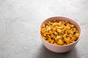 Golden Raisins in a Pink Bowl on a gray background, side view. Copy space.