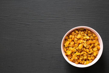 Golden Raisins in a Pink Bowl on a black background, top view. Flat lay, overhead, from above....