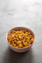 Golden Raisins in a Pink Bowl on a gray surface, side view. Copy space.