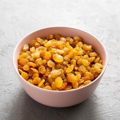 Golden Raisins in a Pink Bowl on a gray surface, side view. Close-up.