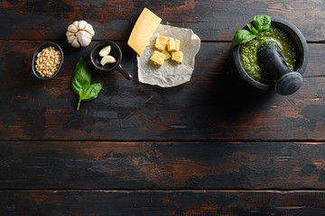 fresh Green basil pesto in mortar  preparation in black mortar with italian recipe ingredients  over old wood table copy space for text overhead.