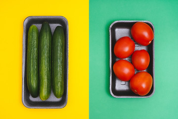 Tomatoes and cucumbers in a black plastic containers on a yellow and green background. Top view. Shiny vegetables.