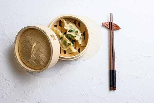 steamed dumpling in traditional wooden steamer on white texture stone background top view