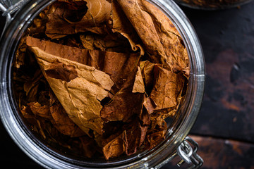 close-up Cigar and pile of tobacco leaves of Dried tobacco  in glass jars on rustic wood dark table...