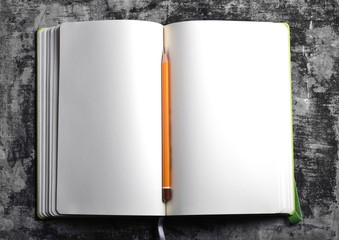 top view of an open book with white blank pages and brown pencil on grey grungy background