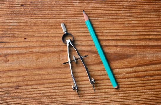 vintage metal drawing compass and green pencil isolated on wooden table