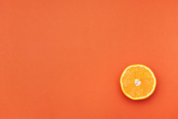 One half of an orange in the corner of an orange background. Copy space. Juicy shiny orange.