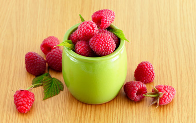 Red, ripe and sweet raspberries in a green bowl on a wooden table